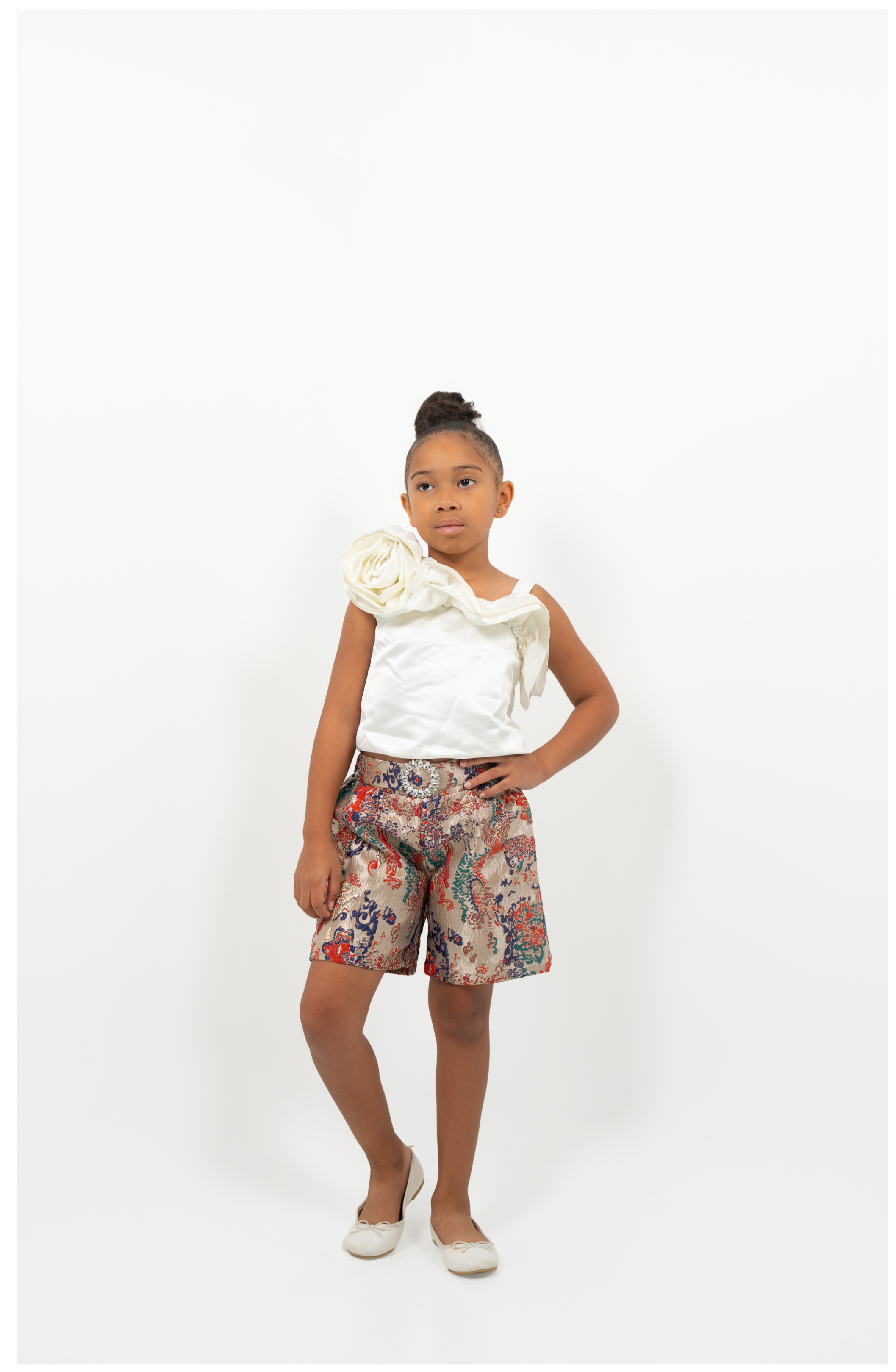Young Girl wearing white satin flower-shoulder top with brocade shorts, styled for elegant party or special occasion